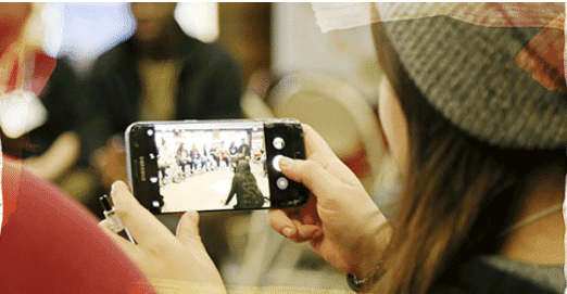 Student is using a smartphone to record or take a picture of a group of people. The scene is captured on the phone's screen.