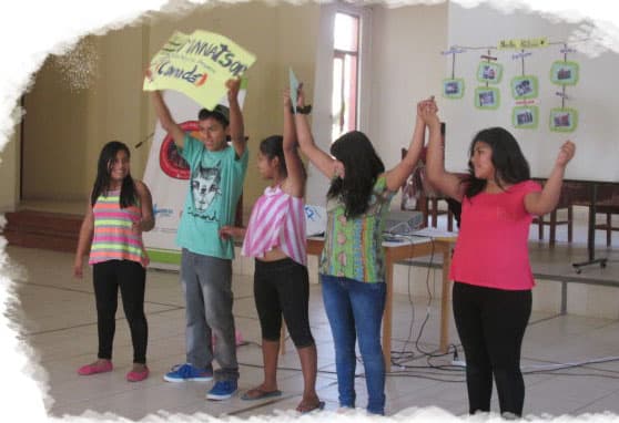 Groupe d'enfants montrant leurs mains peintes en jaune, se tenant fièrement devant une fresque qui souligne l'implication communautaire et l'autonomisation des jeunes.