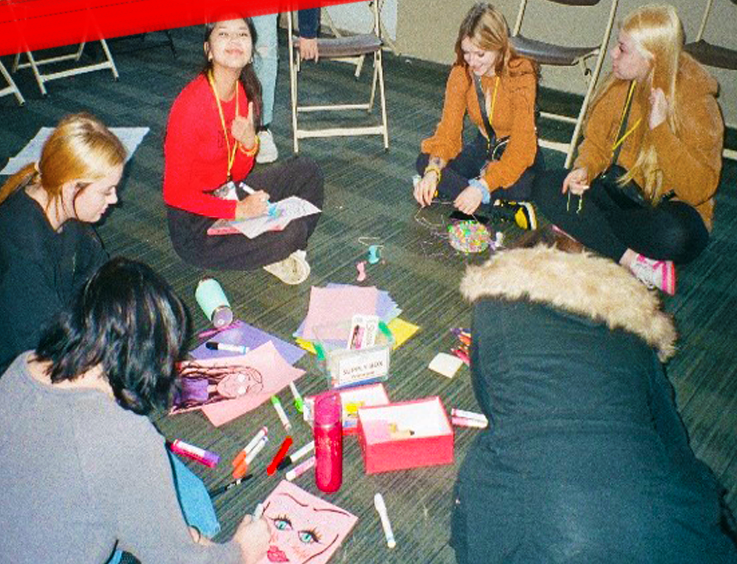 Groupe de jeunes assis en cercle par terre, travaillant sur des projets artistiques avec des marqueurs, du papier et d'autres fournitures.